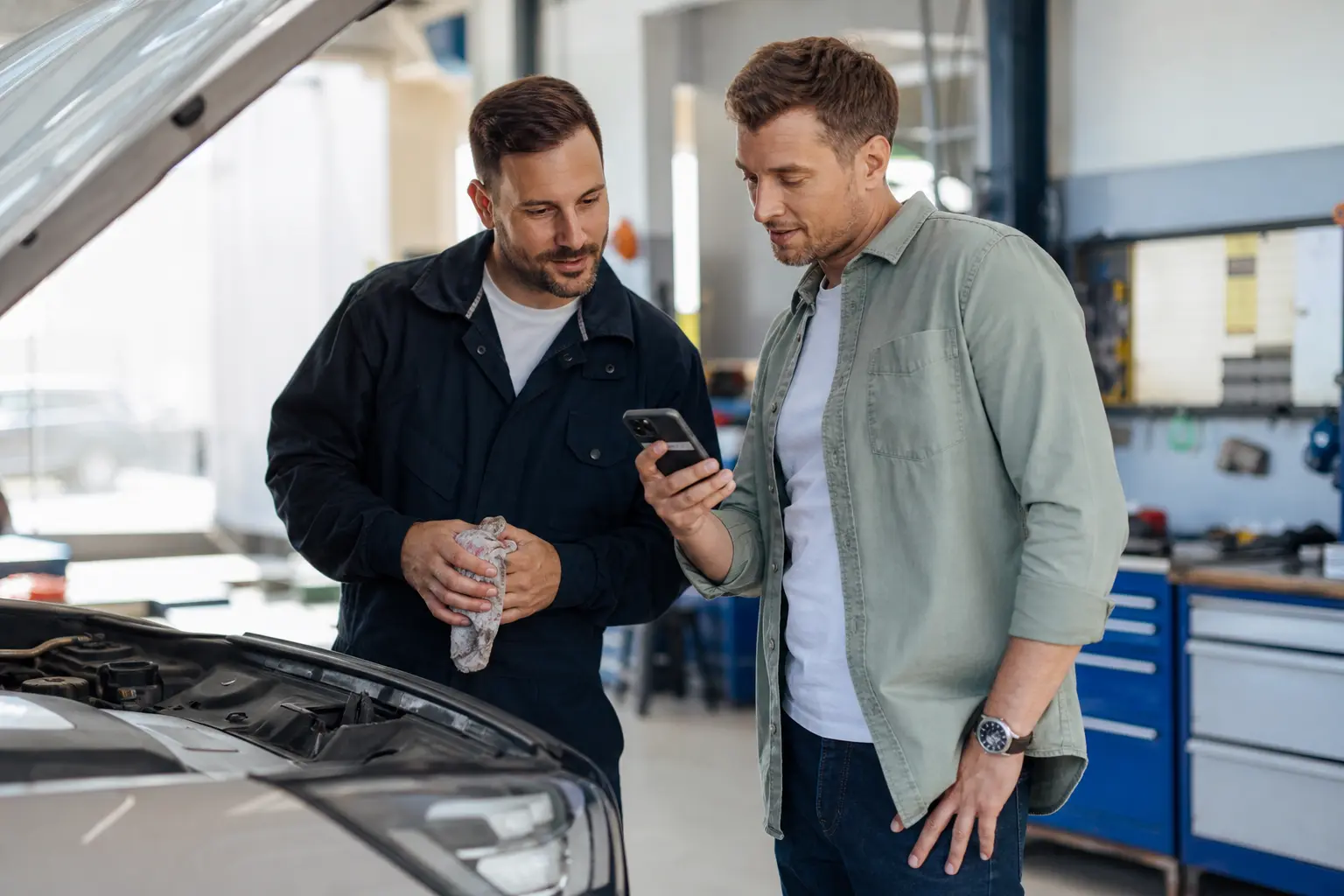 Garage mechanic helping a customer beside a serviced car